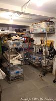 Two wire shelving units in basement with plastic containers and miscellaneous items on shelves. Shows general wear and rust.