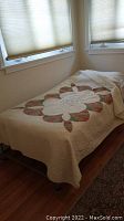 Twin size bed covered with a handmade floral quilt placed near windows on hardwood floor.
