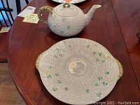 Photo showing teapot and serving platter on wooden table with small note in background