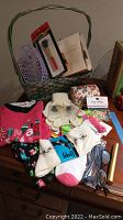 Top view of Christmas pajamas, knit gloves, socks, eyeglasses, makeup brushes with bag, hair clips, and other items on a dark wood surface with a green woven basket.