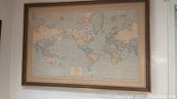 Framed Rand McNally Cosmopolitan World Map hanging on wall, showing full map with wooden frame.