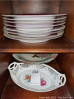 Stack of eight white porcelain dinner plates with subtle floral patterns on the edges, stored on a wooden shelf.