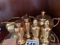 Gold-toned china set with salt and pepper shakers, creamer, and covered sugar bowl, placed on reflective surface.