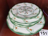 Stack of six dishes showing the lotus flower petal design and green borders with small orange flowers.