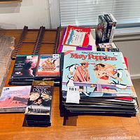 Photo showing stack of vinyl records including unopened Disney's Mary Poppins soundtrack, DVDs, VHS tapes, and sheet music booklets