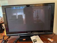 Front view of Panasonic Viera 42-inch plasma HDTV on stand with remote and manual in front.