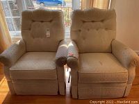 Front view of pair of matching beige fabric upholstered recliners with button tufted backs, showing armrests and seating cushions.