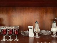 Shelf with ruby red stem glasses, electroplated nickel silver shakers, and cut glass bowls.