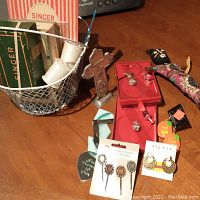 Overall photo of wire basket and contents on wooden surface including sewing boxes, jewelry, cross, and voodoo doll
