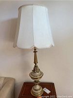 Full lamp showing white fabric shade with scalloped edges and brass body with cream accents on table.