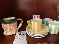 Toby Staffordshire Pickwick character mug and four demitasse espresso cups with matching striped saucers and plate, displayed on wood shelf.