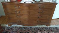 Full front view of vintage wooden dresser with 8 drawers on wheels, placed on a patterned rug.