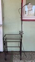 Full view of the nesting tables with one table pulled out, showing glass tops and rust on metal frames along with lamp attached on the side.