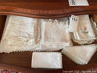 Vintage handmade table linens arranged on wooden table showing variety of napkins and placemats with lace and embroidery detail.