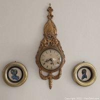 Vintage gilded wall clock centered between two small round silhouette paintings in matching gold frames