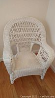 Front view of the white painted wicker armchair showing the full seat and armrests.