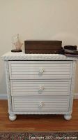 Full view of white wicker dresser showing front with three drawers and items on top.