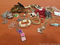 Full view of assorted costume jewelry including bracelets, necklaces, earrings, and watches on a rust-colored cloth.