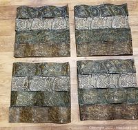 Four metal wall art panels laid flat showing embossed floral motifs and distinct patina colors for each wave section