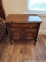 Front angle view of one Drexel Touraine nightstand showing carved panels, brass pulls, and wood grain finish with minor wear.