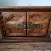 Front view of one vintage Spanish/Mexican provincial nightstand showing carved wood doors and large solid brass pulls.