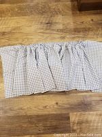 Panel of gingham plaid valance curtain with gathered top lying flat on wood surface, showing fabric pattern and texture.