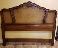Full front view of a vintage mahogany headboard with carved details and caned wicker panels centered and on sides.