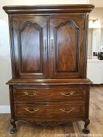 Front view showing two large cabinet doors with carved panels, two curved large drawers below with brass handles, and decorative carved wood details on corners and edges.