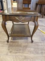 Front view showing the table's cabriole legs, single drawer with brass handle, and cane lower shelf