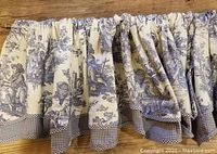 Close-up of vintage French toile pattern in cobalt blue on cream cotton fabric with gathered top and checkered border