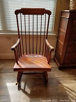 Front angled view of the Nichols & Stone rocking chair showing the Windsor style spindle back and warm wood finish, with natural light highlighting the wood grain.