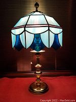 Lamp illuminated showing detailed colors and pattern of the stained glass shade and shiny brass base with finial.