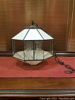 Hexagonal hanging stained glass swag lamp with white opalescent and etched beveled glass panels on a table, attached to a dark metal chain.