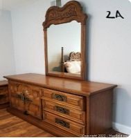Front and right side view of wooden dresser with three deep drawers and cabinet doors. Shows carved panel design and Spanish/Mexican style brass pulls. Mirror attached on top with carved decorative wood frame.