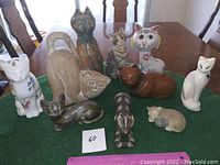 Ten cat figurines displayed on green mat on table surface, showing various materials and finishes.