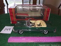 Green diecast model of 1955 Buick Century convertible with cream interior, ruler for scale, original MIRA box behind.