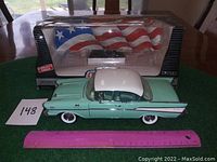 Diecast model car displayed outside box showing side profile with ruler for size reference.