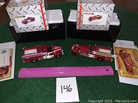 Two die-cast fire truck models displayed with original boxes, paperwork, and a pink ruler for scale.