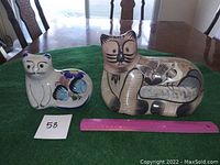 Two hand painted Manzanillo ceramic cat figures placed on a green cloth on a table with ruler for size reference, showing front and side views.