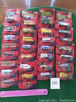 Full view of 30 vehicles in original red card packaging arranged on green background with ruler for scale and label 135 visible.