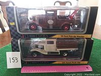 Two die cast metal models in black and silver boxes, showing a brown 1934 Ford Pick-Up Wrecker on top and a white 1934 Ford Pick-Up truck below, both unopened.