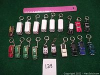 Top down view of all 19 Kinsmart car keychains arranged in rows with a pink ruler for scale.
