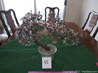 Front view of large artificial jade tree with pink and white flowers set on a green cloth on a table.