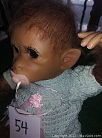 Close-up of monkey baby doll face showing detailed features like eyes, nose, mouth with pacifier, fuzzy hair, and ears.