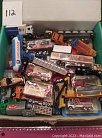 Overview photo of assorted toy vehicles stacked inside a box showing multiple models including tanker trucks and flatbed trucks.