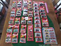 Overview showing multiple rows of Tonka die cast vehicles in unopened packaging on a table surface, including trucks, tractors, fire trucks, and construction equipment with a pink ruler for scale.