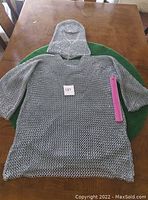 Hauberk tunic and coif laid flat on table with ruler for scale