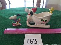 Front side of Vintage 1972 Snoopy and Woodstock Christmas sled ceramic dish with Snoopy figurine on skis beside it, ruler for scale.