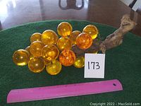 Photo showing the full cluster of amber glass grapes with natural wood stem lying on a table with green cloth background and pink ruler for size reference.