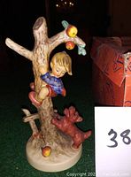 Photo shows the front and side view of the Goebel Hummel figurine, a child climbing a tree with an excited dog and apples around.